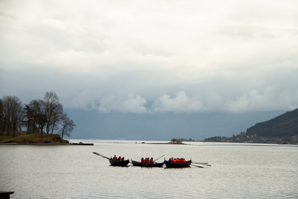 Tre robåtar med folk ute på fjorden i overskya vær. 