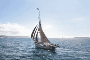 Traditional wooden sailing boat on the fjord in Hardanger and Voss, Norway, with scenic mountain views, showcasing maritime history at Hardanger og Voss Museum, Norway.